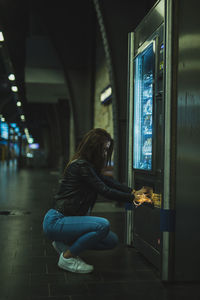 Side view of young woman holding illuminated string light opening refrigerator in store at night
