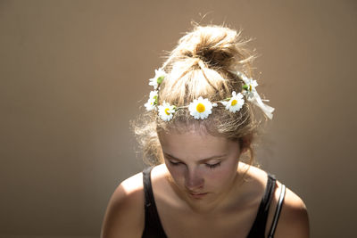 Teenager wearing white flowers on head against beige wall