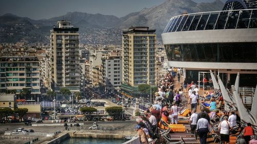 Crowd and lounge chairs on cruise ship against city