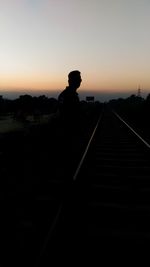 Silhouette man standing on railroad tracks against clear sky during sunset