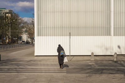 Rear view of woman walking on footpath against building