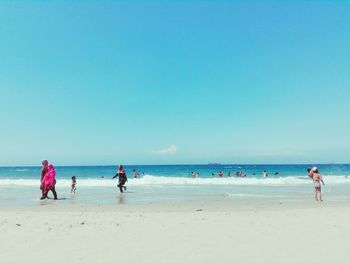 People on beach against clear blue sky