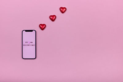 Smartphone and heart-shaped candies on pink background