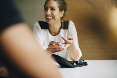 Smiling businesswoman doing blood sugar test while sitting with colleague at table in office