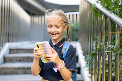 Portrait of smiling girl holding smart phone while standing outdoors