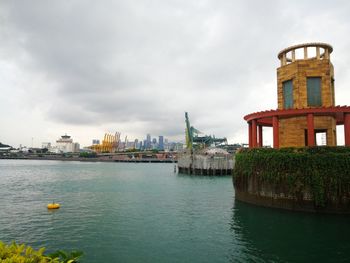 Buildings at waterfront against cloudy sky