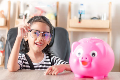 Portrait of girl sitting by piggy bank at table