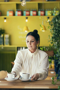 Owner picking coffee cups against wall at cafe