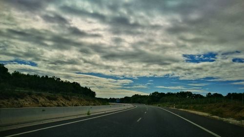 Road passing through landscape against cloudy sky