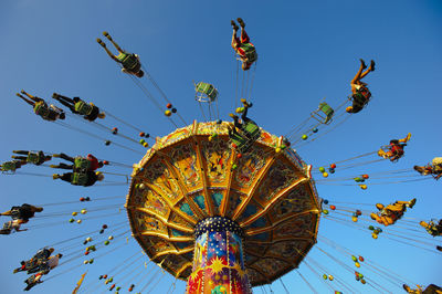 Low angle view of people sitting in carousel against clear blue sky