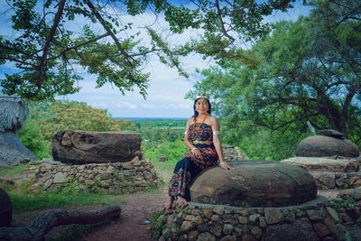 Young woman sitting on rock against trees wearing sabu island traditional clothes 