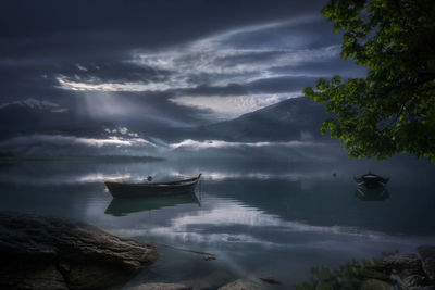Boats moored in lake against cloudy sky