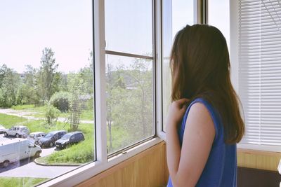 Side view of woman looking through window at home
