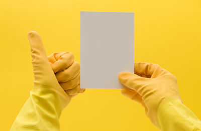 Cropped hand of woman holding paper against yellow background