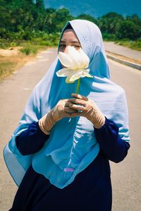 Portrait of young woman wearing hijab holding flower on road