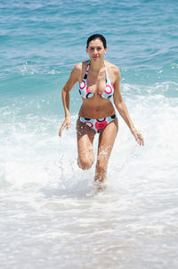 Seductive woman wearing bikini running in sea during sunny day