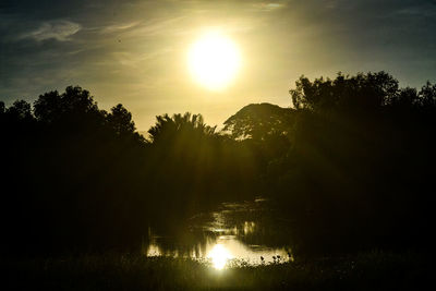 Silhouette trees by lake against sky during sunset