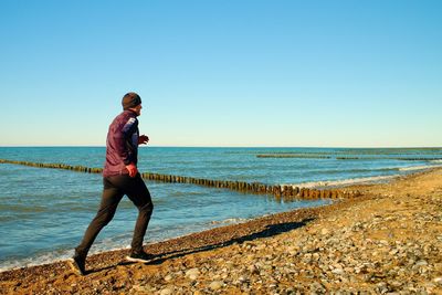 Tall man in dark sportswer running and exercising on stony beach at breakwater. vignetting effect