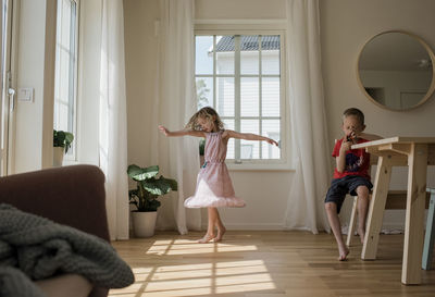 Young girl dancing at home whilst her brother plays