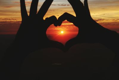 Silhouette hand holding heart shape against sunset sky