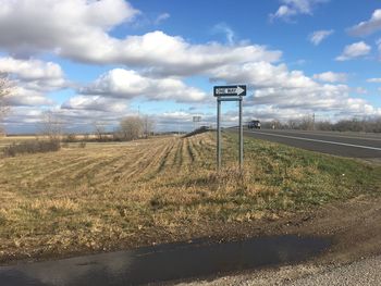 Road sign on field against sky