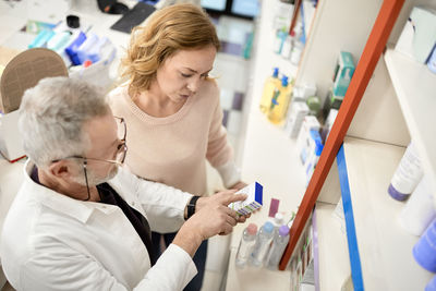 Pharmacist helping customer reading instruction on medicine box at pharmacy store