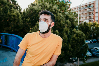 Man wearing mask standing by railing against trees