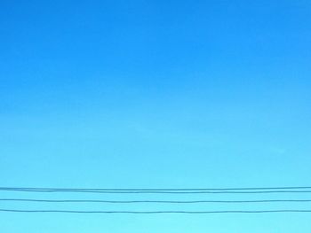 Low angle view of power lines against clear blue sky