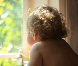 Rear view of shirtless man looking through window