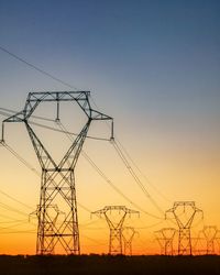 Low angle view of electricity pylon against clear sky during sunset