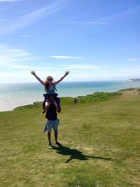 Young man carrying girlfriend on shoulders while standing against sea