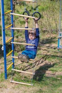 A blonde-haired child is playing on the playground, hanging on rings