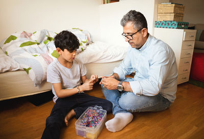 Father and son playing with rubber bands while sitting on hardwood floor at home