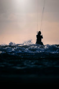 Silhouette person by sea against sky during sunset