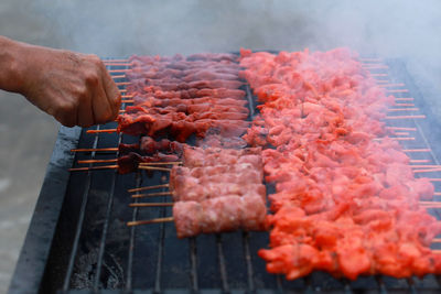 Close-up of hand holding meat on barbecue grill