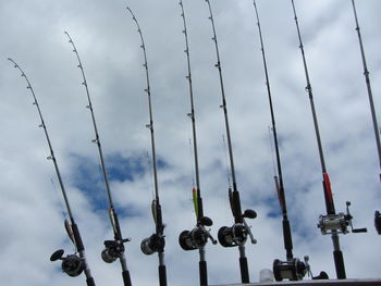 Low angle view of fishing rods against cloudy sky