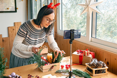 Female florist blogger making winter ikebana with pine branches, candle and christmas decorations