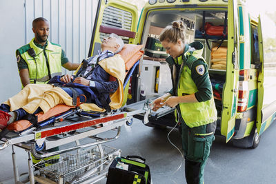 Paramedic with patient looking at coworker preparing oxygen equipment outside ambulance