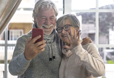 Portrait of senior couple doing selfie while standing by window at home