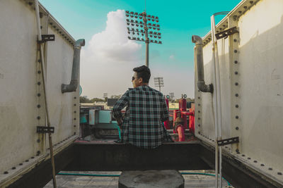 Rear view of woman sitting on metal against sky