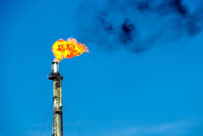 Low angle view of smoke stack emitting fire against sky