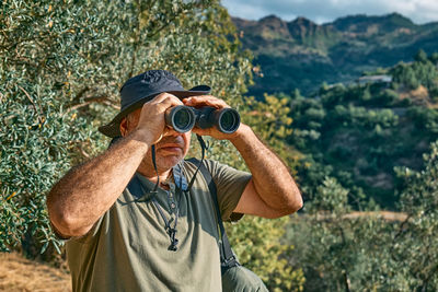 Tourist man looking through binoculars at the mountains view. traveling or exercising outdoors. 