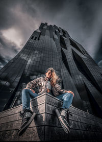 Low angle view of woman sitting against modern building