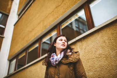 Portrait of young woman looking away while standing against building