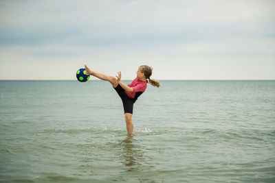 Cheerful boy playing with ball in sea