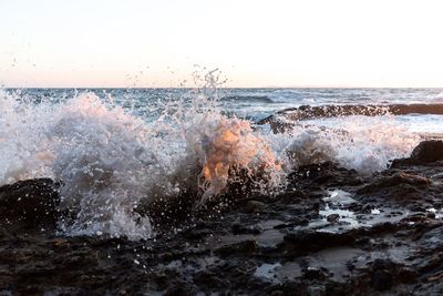 Waves splashing on rocks against clear sky