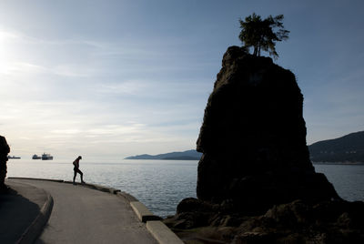 Man standing on rock by sea against sky