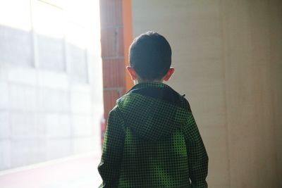 Rear view of boy standing by window at home