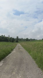 Road passing through agricultural field against sky