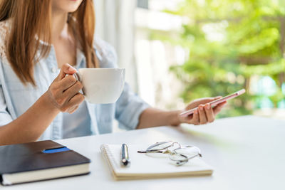 Midsection of woman holding coffee while sitting on table